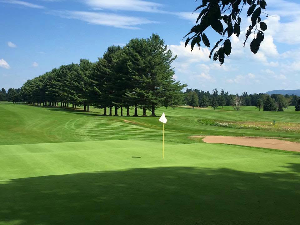 A manicured green framed by tall pines and Adirondack mountains at Saranac Inn Golf Club