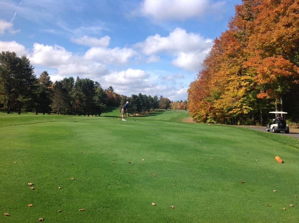 A Saranac Inn fairway lined with early-autumn color under a blue Adirondack sky