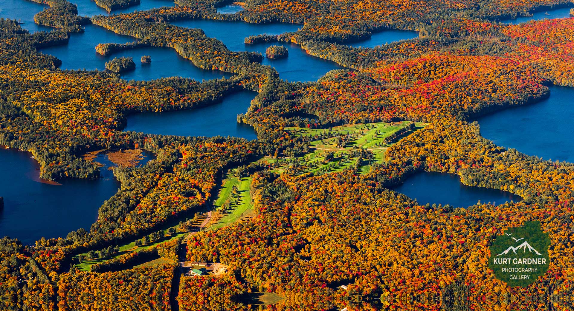 Aerial view of Saranac Inn Golf Club threading the Adirondack lakes in peak fall color
