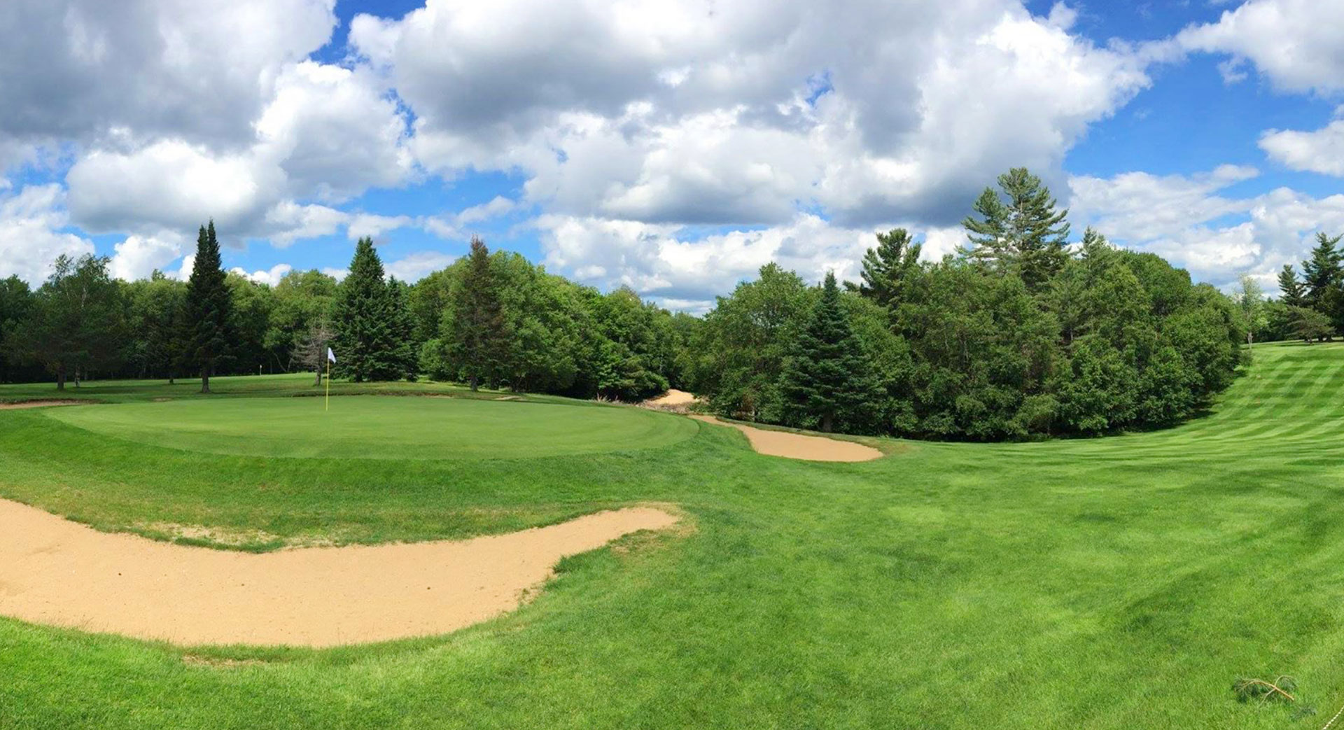 A fairway green framed by pines and bunkers under a bright Adirondack sky at Saranac Inn Golf Club